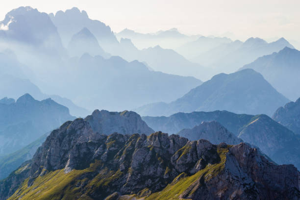 Photo of Layers of silhouettes of mountain ridges and peaks in the Italian Alps, at sunset. View from the route down from Mangart (Mangrt) peak, Julian Alps, Triglav, Slovenia.