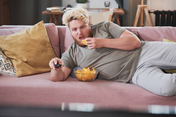 Lazy man eating potato chips and watching TV stock photo
