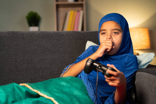 Lazy muslim girl kid playing video game by using joystick or gamepad at home while sleeping on sofa at home play game sleep stock pictures, royalty-free photos & images