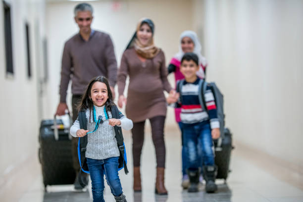 Leading The Family A Middle-eastern father, mother, brother and two sisters have just arrived to their new apartment building. They are carrying their luggage with them. They are walking down the hallway, being lead by the happy youngest daughter. immigrant stock pictures, royalty-free photos & images