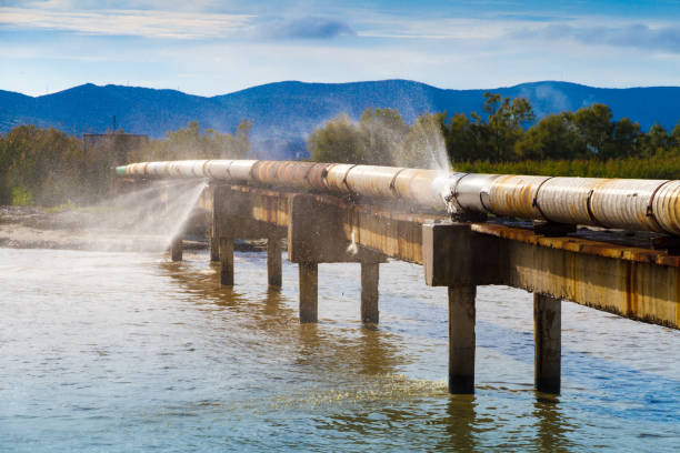 A leaking pipeline in the sun crossing a canal. A leaking pipeline in the sun crossing a canal near the shoreline Burst Pipe stock pictures, royalty-free photos & images