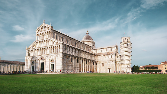 Leaning Tower of Pisa (elaborately adorned 14th-century tower) and Cathedral di Pisa (marble-striped cathedral) on summer green grass and blue sky. Travel Italy, famous places. Color graded