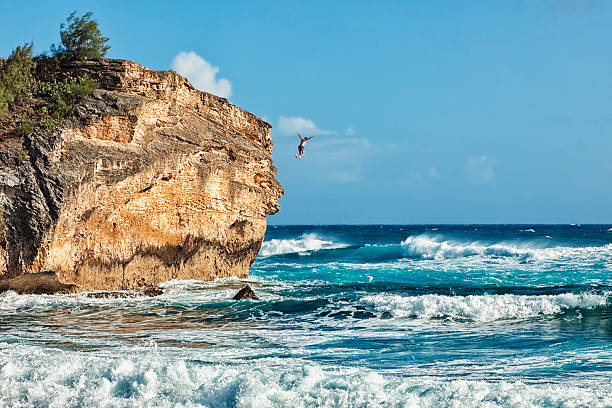 Leap of Faith: Cliff Jumper "Photo of a man jumping into the ocean from the top of Makawehi Point at Keoniloa Beach (aka Shipwreck Beach), Kauai, HI." cliff jumping stock pictures, royalty-free photos & images