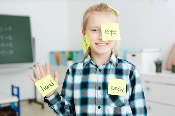 Learning body parts Happy schoolgirl having sticky notepapers with English names of body parts on her hand, cheek and eye english language stock pictures, royalty-free photos & images