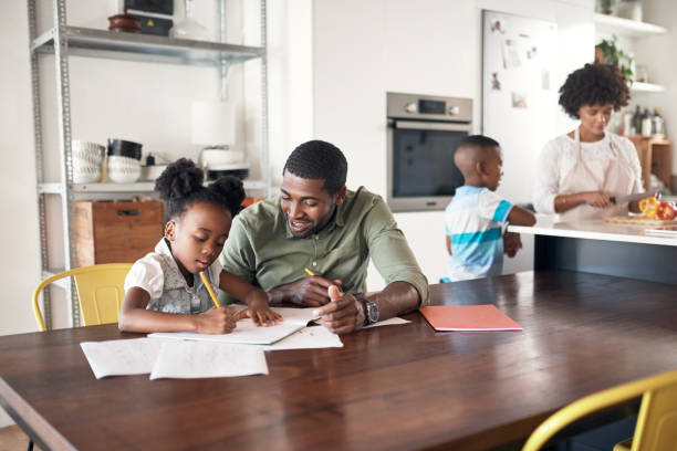 Learning isn't only for school Shot of young man helping his daughter with her homework while her mother cooks in the background homework stock pictures, royalty-free photos & images