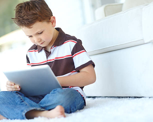 A cute little boy using a digital tablet while sitting at home
