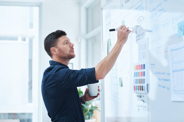 Leave the creative work to me Shot of a handsome mature male designer working on a whiteboard in the office whiteboard visual aid stock pictures, royalty-free photos & images