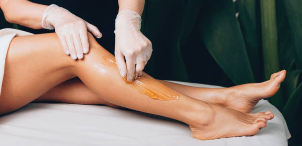 Leg waxing procedure at the spa salon with a caucasian woman lying on bed stock photo
