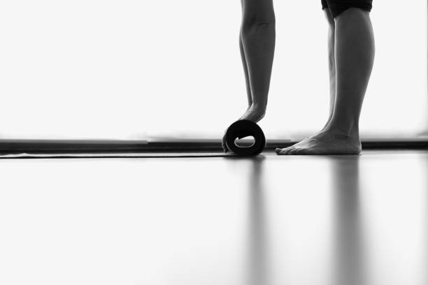 Legs and hands of woman folding yoga mat in bright studio room Yogi rolling equipment after morning practice. Pilates, natural light floor reflection, minimalism concepts. Black and white photography barefoot photos stock pictures, royalty-free photos & images