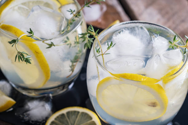 Lemon cocktail with thyme and ice on dark rustic background, close-up. Refreshing alcoholic yellow cocktail drink. stock photo