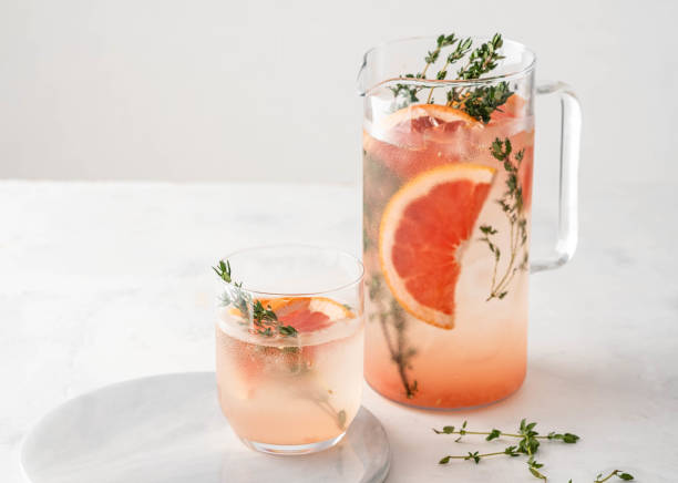 Lemonade with grapefruit and thyme in a glass jug on light background. stock photo