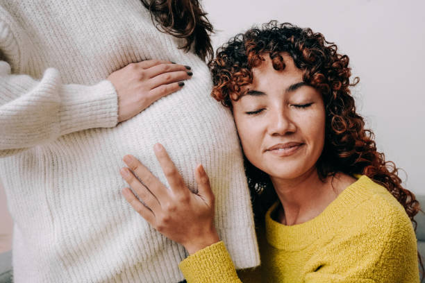 LGBT lesbian pregnant woman having tender moment listening her wife baby belly - Focus on right female stock photo