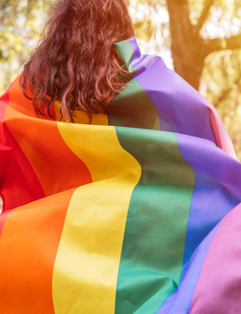 Lesbian woman wearing an LGBTQ flag, symbol for the homosexual community, as a cape. Gay rainbow colors flag for pride month and the celebration day of sexual and love diversity stock photo