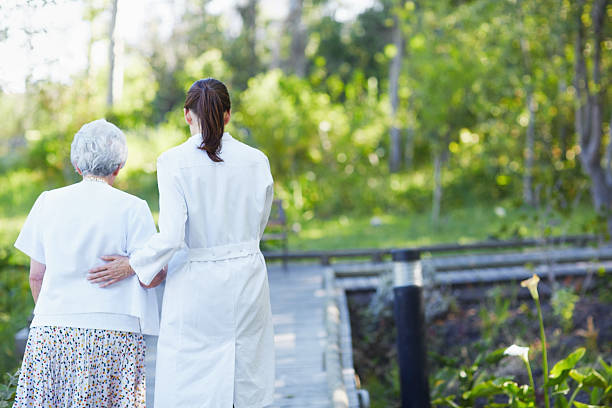 A rear view of a caregiver guiding an elderly woman during a stroll...
