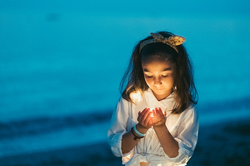 Little girl holding lights in hands cupped and making a wish at night