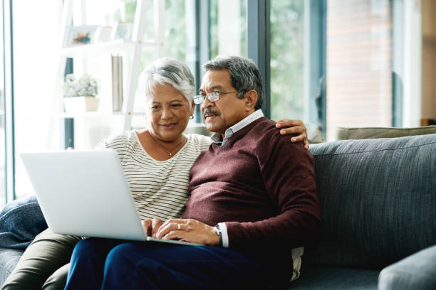 Let's look at restaurant reviews online and pick from there Shot of a mature couple using a laptop while relaxing at home looking stock pictures, royalty-free photos & images