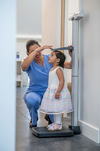 A female nurse is taking her young patient's height measurement using a stadiometer at the hospital.