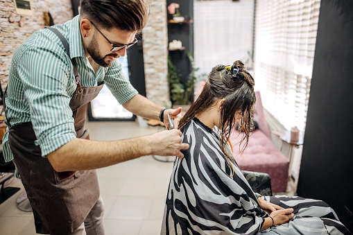 Handsome male hairdresser styling and treating a woman's hair inside a salon