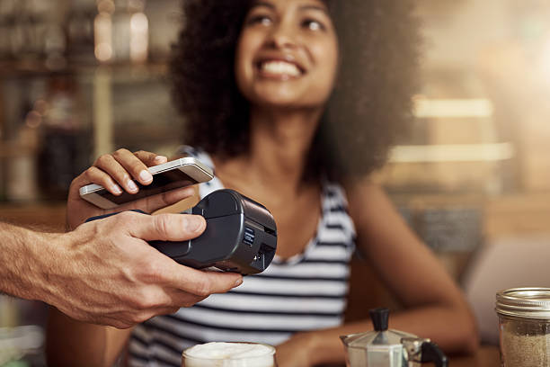 Life's getting easier! Shot of a beautiful woman using her smart phone and an electronic reader to pay her bill in a coffee shop contactless payment stock pictures, royalty-free photos & images
