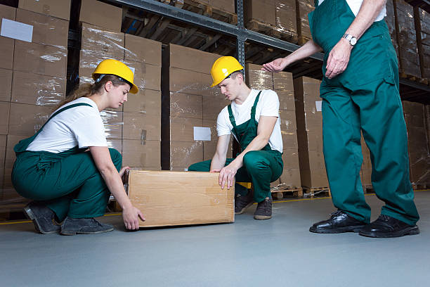 Lifting the box Two young workers lifting heavy box in warehouse picking up stock pictures, royalty-free photos & images