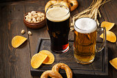 Light and dark beer with various snacks - chips, pretzels and nuts on a dark wooden background. Copy space.