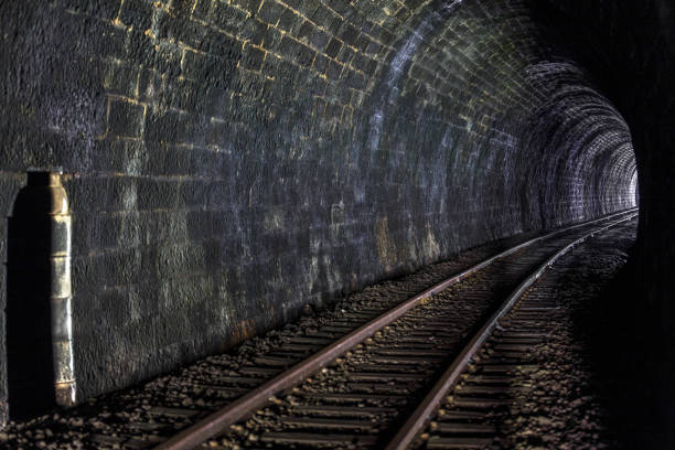 Light at the end of a dark tunnel with rail tracks stock photo