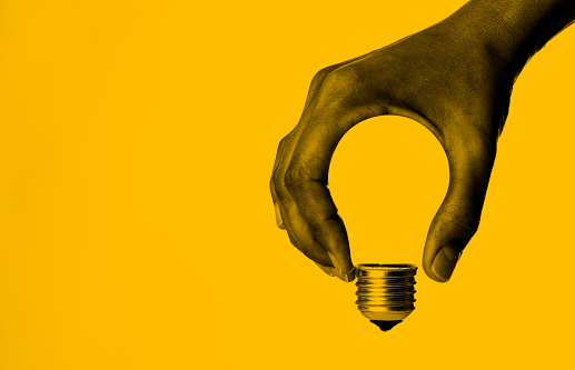 Light bulb in human hand, yellow background.