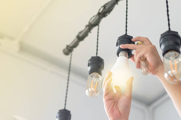 led light power saving concept. asia man changing compact-fluorescent (cfl) bulbs with new  bulb. - eletricidade imagens e fotografias de stock