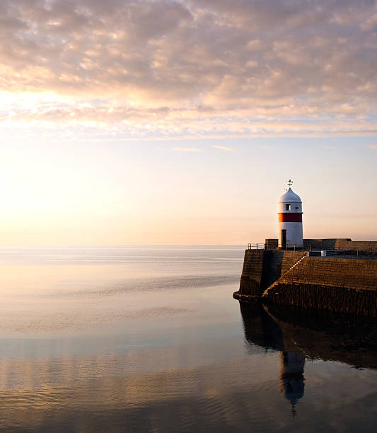 Lighthouse on breakwater wall with calm sea during sunrise stock photo