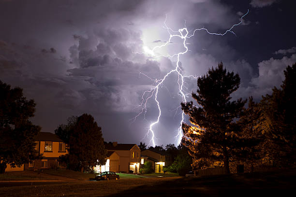 Lightning bolt and thunderhead storms over Denver neighborhood homes A massive thunderhead pours rain and lightning over suburban Denver homes, Colorado. Trees are silhouetted and homes are lit by incandescent light. The thunderhead is lit by huge lightning bolts reaching from the top of the clouds to the ground. thunderstorm stock pictures, royalty-free photos & images