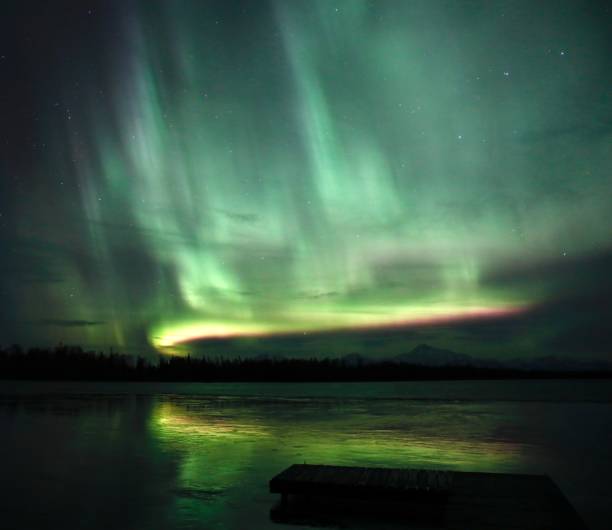 Lights Over the Dock Northern Lights dance across the Alaska night sky above Denali while reflecting on a lake and illuminating a dock. geomagnetic storm stock pictures, royalty-free photos & images