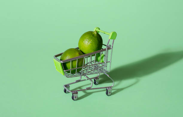 Limes in supermarket cart. Food shopping. Buying citrus fruits Two lime in a miniature shopping cart, isolated on a green background. Food shopping concept. Sale concept. Buying fresh fruits. Healthy eating. aqua menthe photos stock pictures, royalty-free photos & images