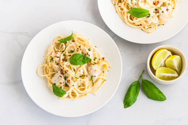 Linguine Pasta in White Sauce Garnished with Basil and Lemon on White Background, Italian Food Photography stock photo