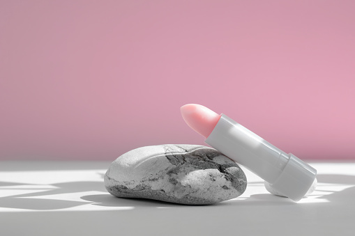 Lip skin care. Close-up of lipstick lip protector on stone, on white pink background, with sun shadow. Beauty cosmetics concept. Spring or summer sunscreen or moisturizing cosmetics.