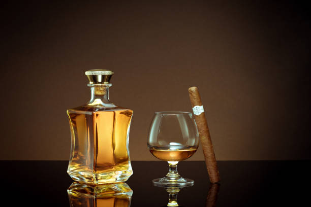 liquor and cigar close up view of cigar, bottle of cognac and a glass aside on color back. brandy stock pictures, royalty-free photos & images