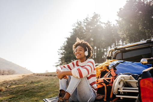 Photo of a young smiling woman listening music while on a road trip