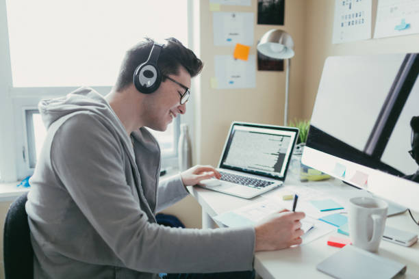 Listening to music and working Young man working from his dorm room while listening to music on his headphones. college dorm stock pictures, royalty-free photos & images