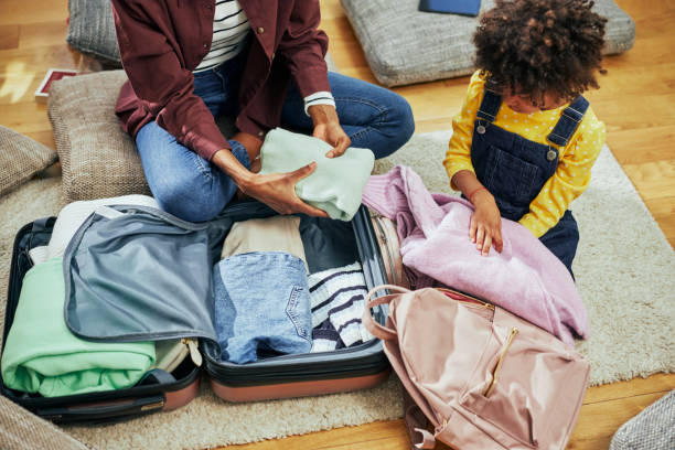 Little African American girl helping her mother pack her suitcase stock photo