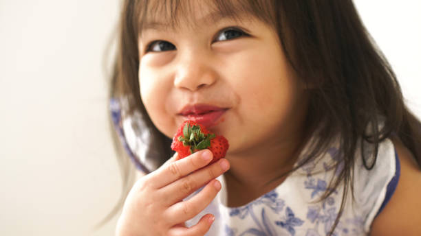 Little Asian baby girl is eating strawberry at her room Little Asian baby girl is eating strawberry at her room cute thai girl stock pictures, royalty-free photos & images
