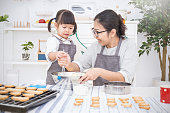 小さなアジアの女の子と彼女の母親は台所でケーキやクッキーを焼く。幸せな家族と motherâs の日のコンセプト