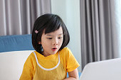 自宅でラップトップコンピュータを使用してオンラインで小さなアジアの女の子の学生の研究