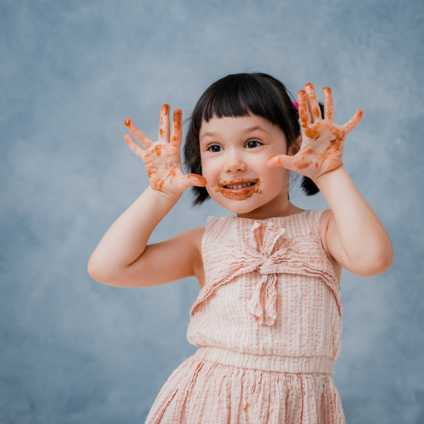 little baby girl eats chocolate and licks her finger on a grey blue Studio background. free space. stock photo