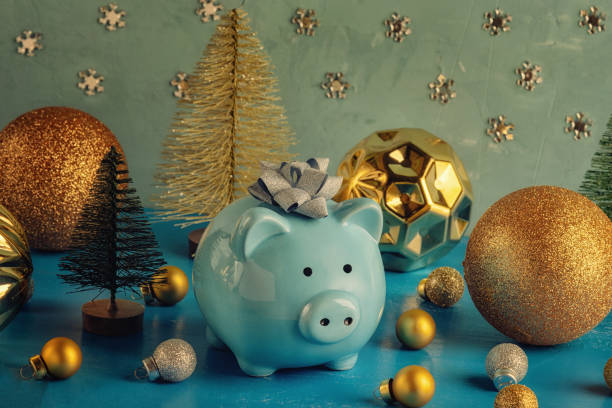 Little blue piggy bank with a bow on his head. Nearby are small decorative Christmas trees and a lot of golden balls of different sizes. The symbol of the new year. Holiday photography. stock photo