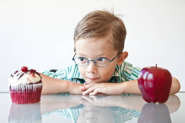 Little boy choosing between a cupcake and apple stock photo