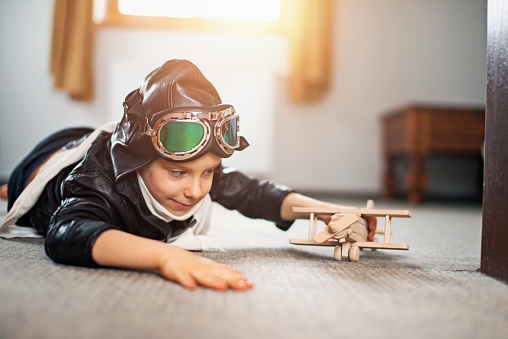 Little boy dressed up as pilot playing with toy plane