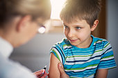 Little boy preparing to have a vaccination injection. The smiling boy is looking at the doctor that is holding a syringe next to his arm.