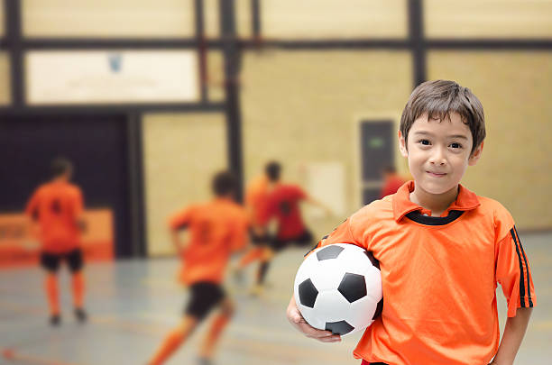 little boy holding football in futsal gym - futsal imagens e fotografias de stock