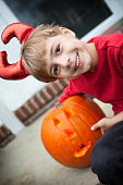 An adorable 6 year old boy dressed as a devil and holding a jack-o-lantern.