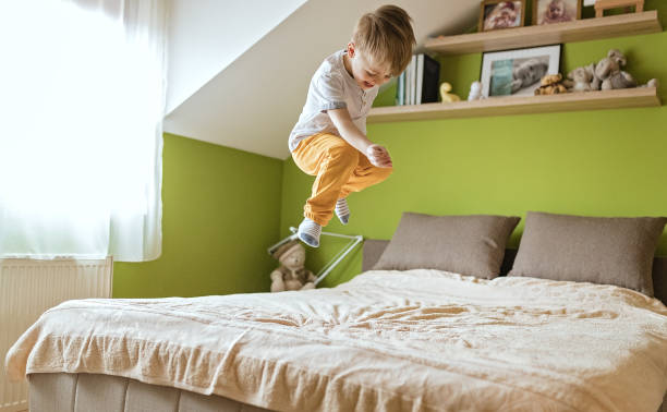 Little boy jumping on the bed Little boy jumping on the bed in his bedroom, trying to fly. boy jumping stock pictures, royalty-free photos & images