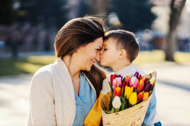 A little boy kissing his mom in the park on mother's day and giving her flowers. stock photo